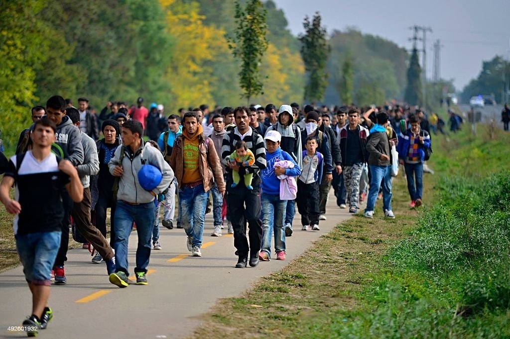 Esta imagen muestra a un grupo de migrantes en caravana, caminando juntos en un camino rural. Los migrantes se enfrentan a un viaje peligroso y lleno de incertidumbres en busca de mejores condiciones de vida. Esta imagen resalta la complejidad y diversidad de las situaciones y motivaciones de los migrantes, y la necesidad de un diálogo constructivo sobre la migración. La migración es un tema complejo y polarizante, y esta imagen puede ayudar a crear conciencia sobre los desafíos que enfrentan los migrantes en su búsqueda de seguridad y oportunidades